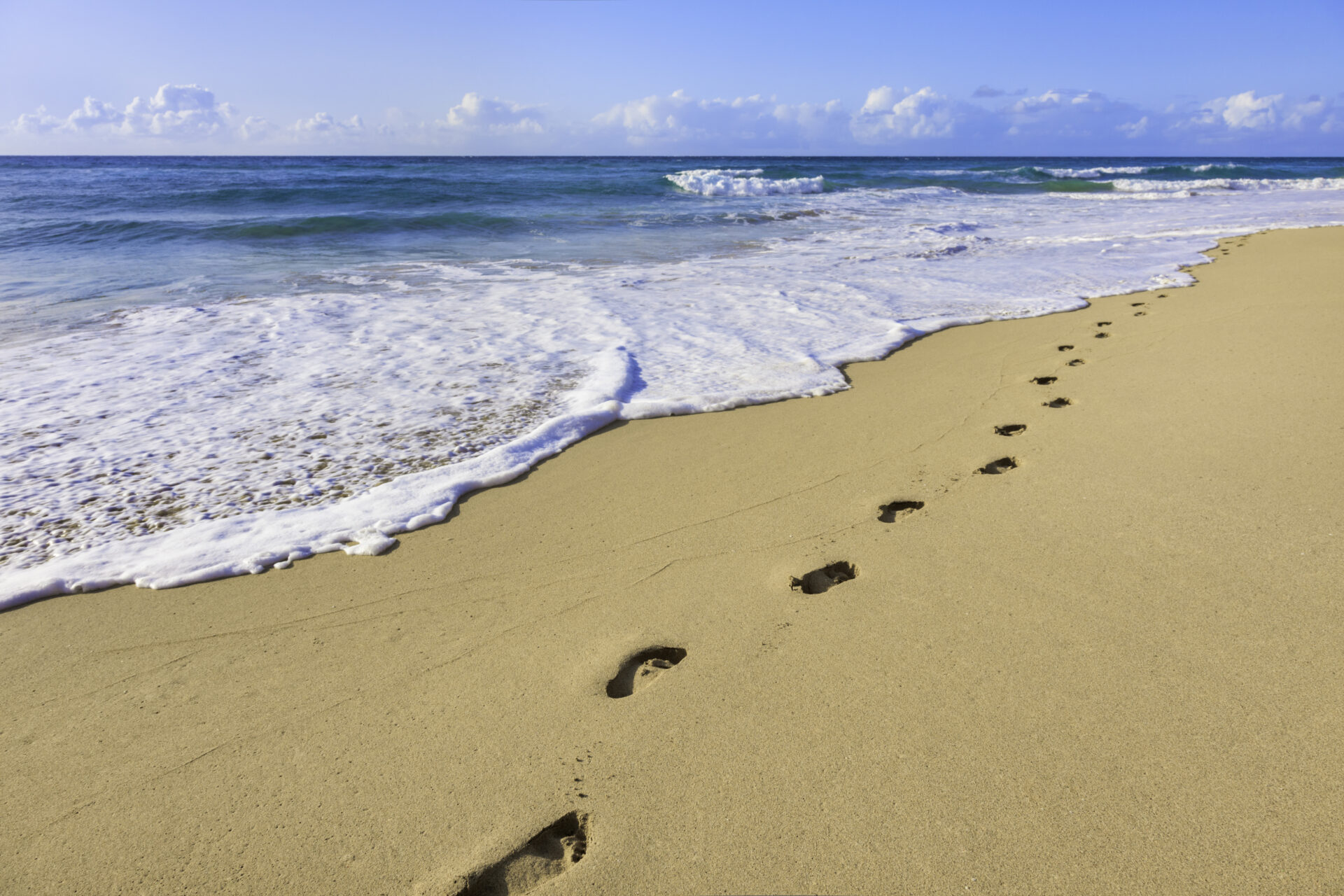 footprints and surf on tropical beach, Kauai, Hawaii